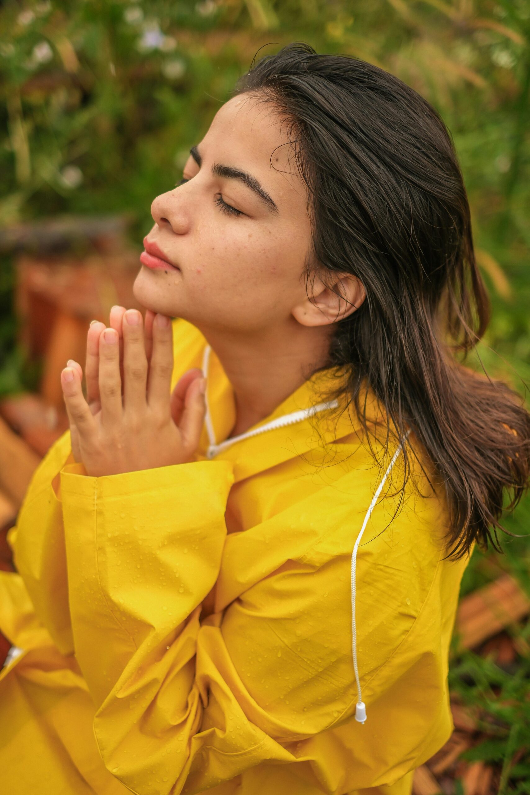 Young woman in a yellow raincoat, eyes closed, enjoying a peaceful moment outdoors.