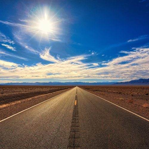 pexels-photo-1133505-1133505 A long, straight road stretches across a dry desert landscape under a bright blue sky and shining sun.