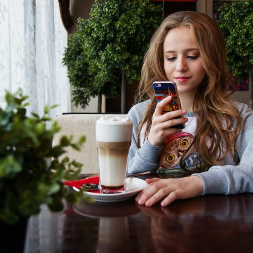 pexels-photo-248021-248021 A young woman enjoys a latte while browsing her smartphone in a cozy cafe.